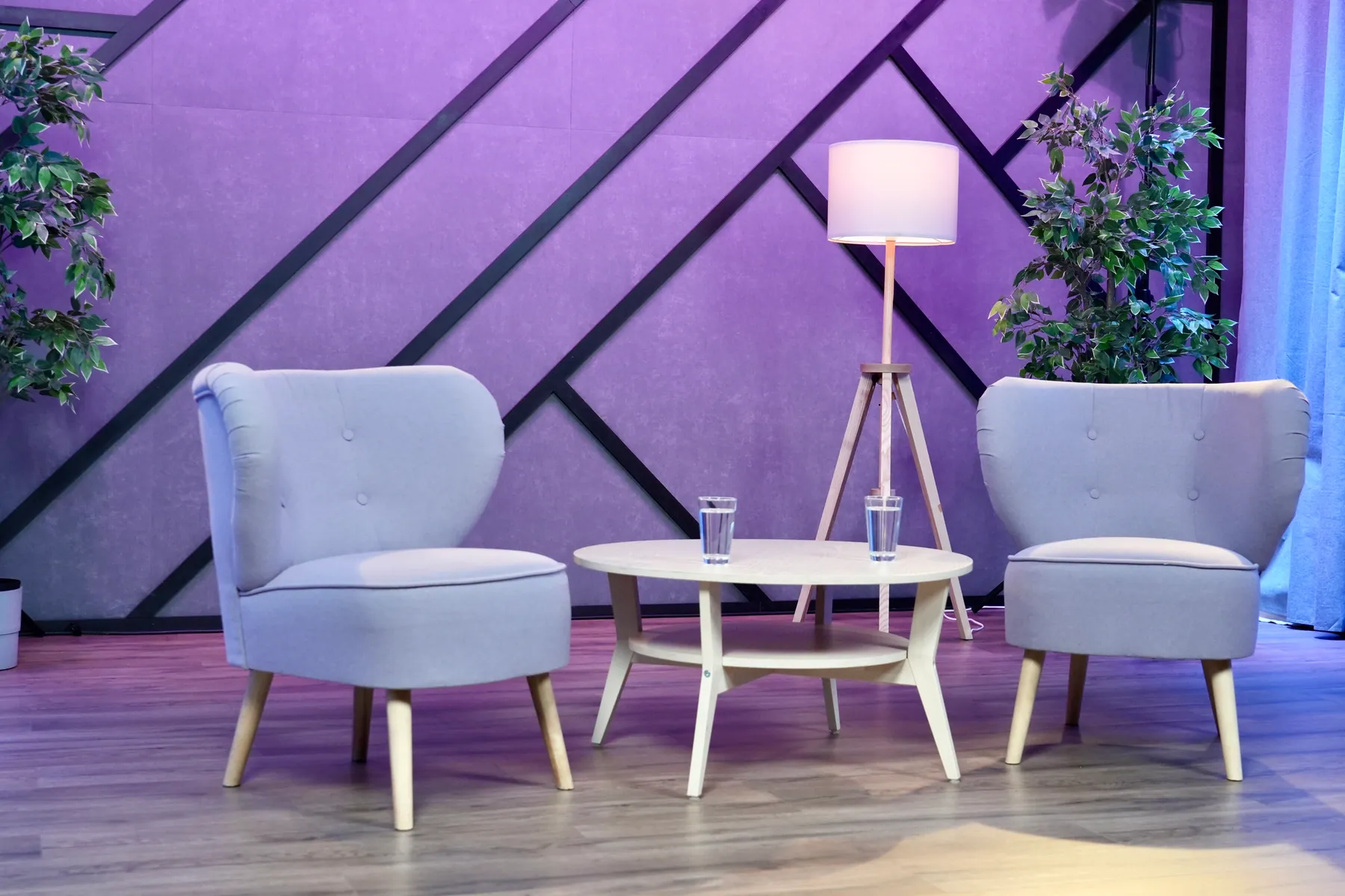 Dwa jasne fotele, stolik i lampa na fioletowo oświetlonym planie Studio 2